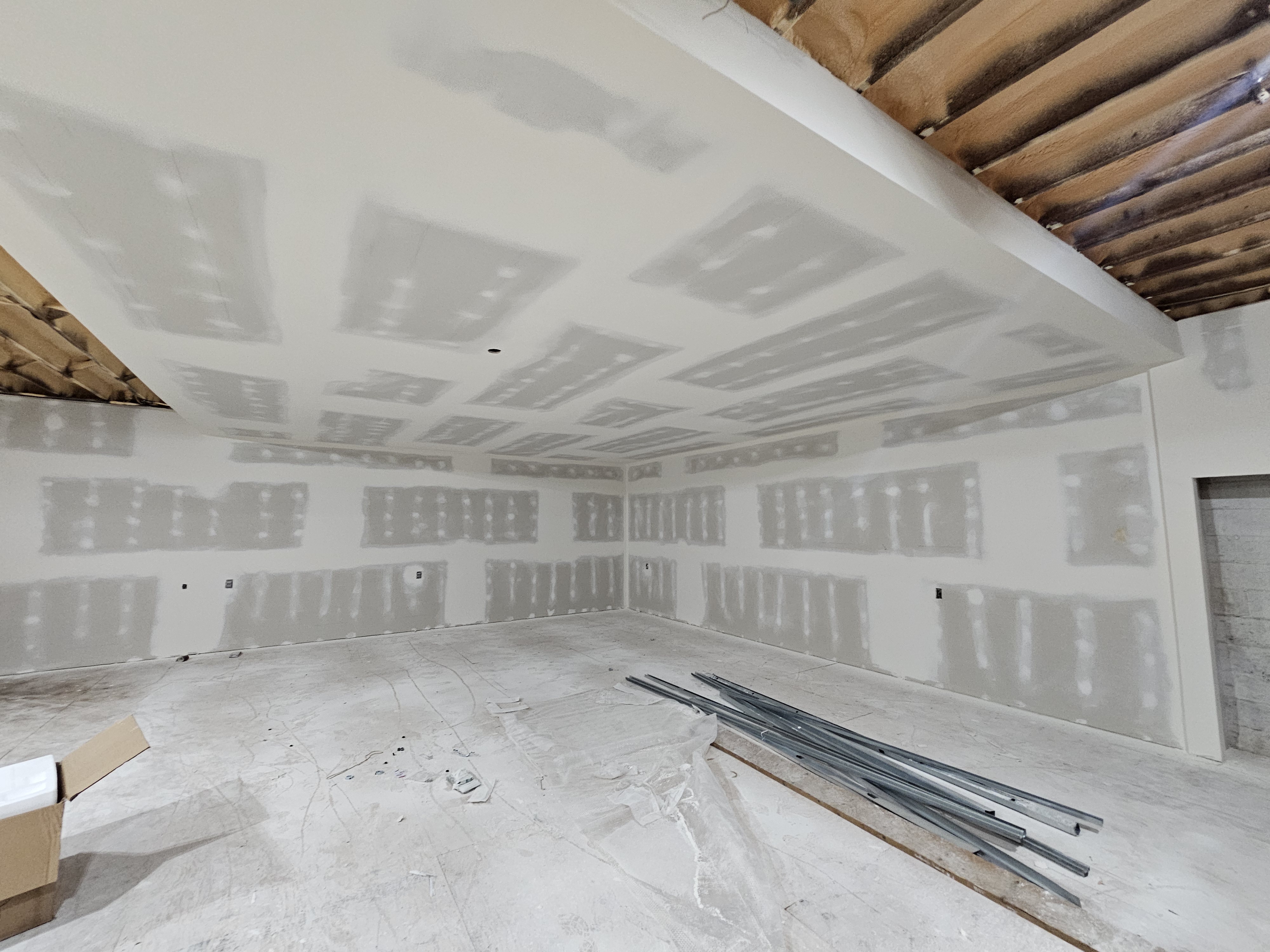 Large room with taped drywall and exposed wood beams